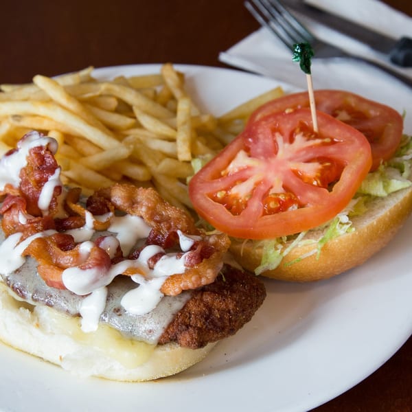 A Town Pub burger with bacon, cheese, and white sauce, served with fries and a side of lettuce and tomato.