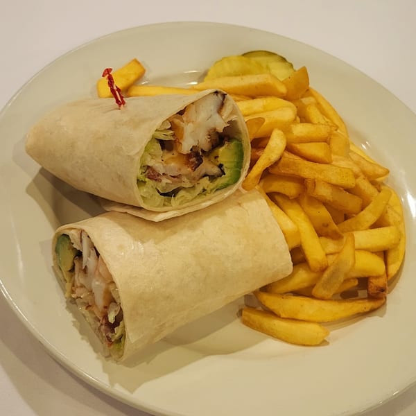 Two fish wraps with avocado and lettuce, served with golden french fries and a pickle.