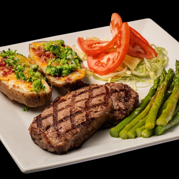Grilled steak with loaded baked potatoes, asparagus, and a side salad on a white plate.