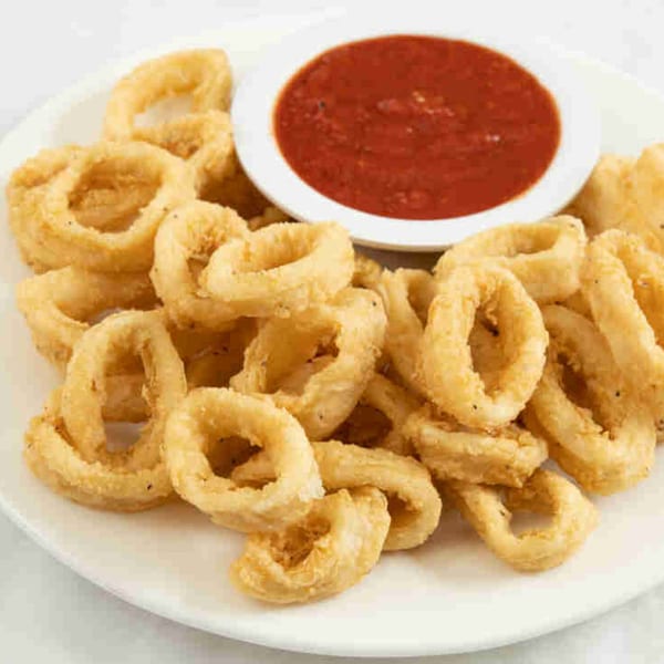 Golden fried calamari rings with a side of red marinara sauce on a white plate.