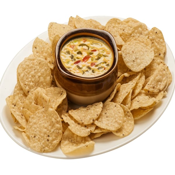 A white oval platter filled with tortilla chips surrounding a bowl of queso dip with peppers.