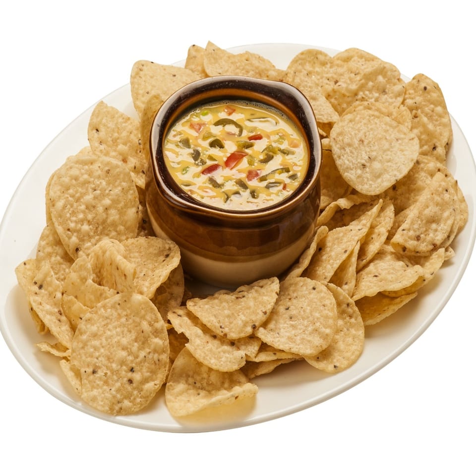 A white oval platter filled with tortilla chips surrounding a bowl of queso dip with peppers.