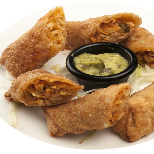 Golden-brown egg rolls with a savory filling, served with a side of green dipping sauce.