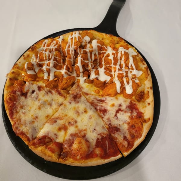 Half cheese and half buffalo chicken pizza with ranch drizzle on a black pan.