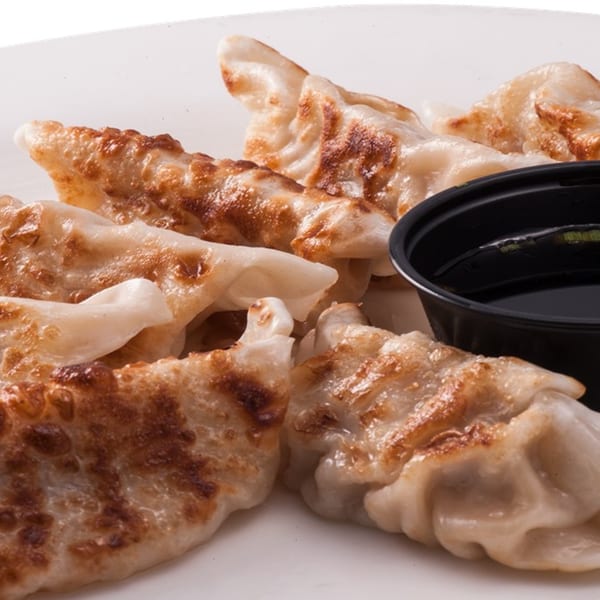 Pan-fried dumplings with crispy bottoms and a side of soy sauce in a black cup.