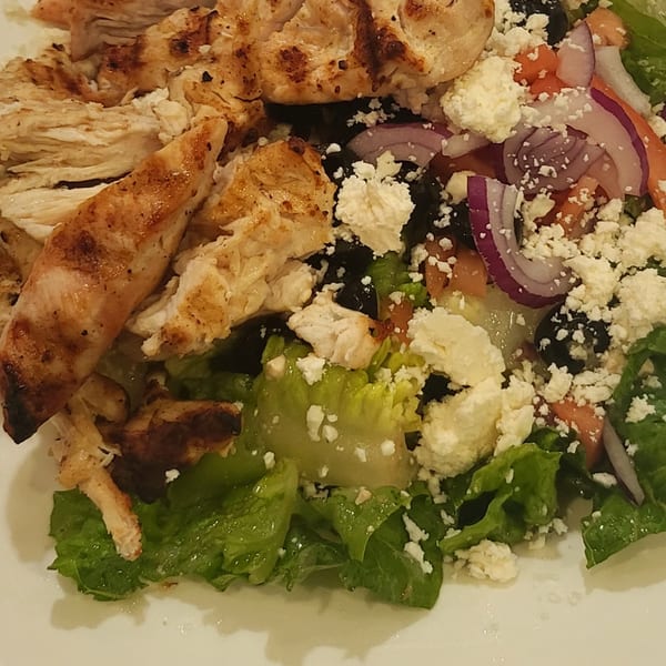 Grilled chicken salad with lettuce, red onions, tomatoes, black olives, and feta cheese.