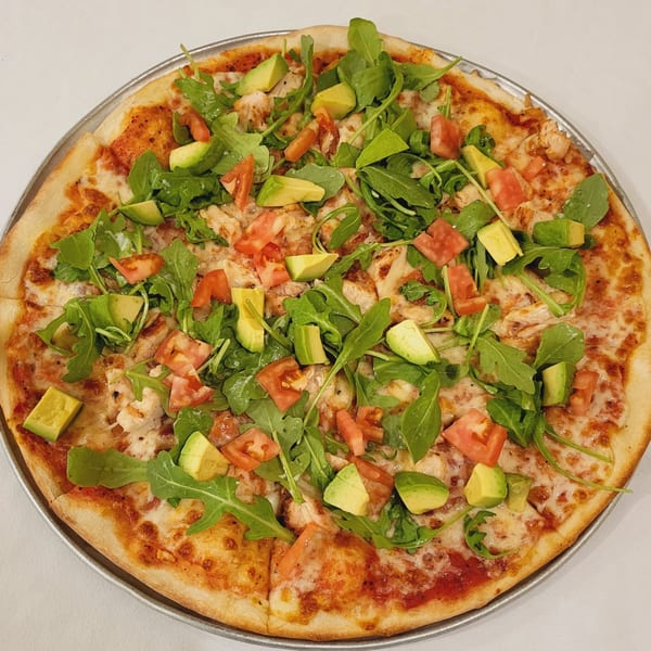 Town Pub's pizza topped with chicken, arugula, diced tomatoes, and avocado on a metal pan.
