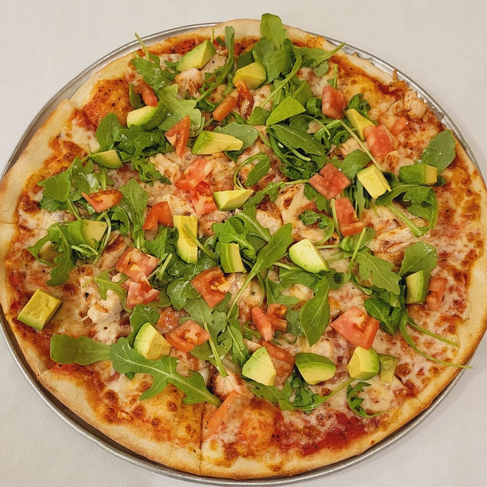 Town Pub's pizza topped with chicken, arugula, diced tomatoes, and avocado on a metal pan.