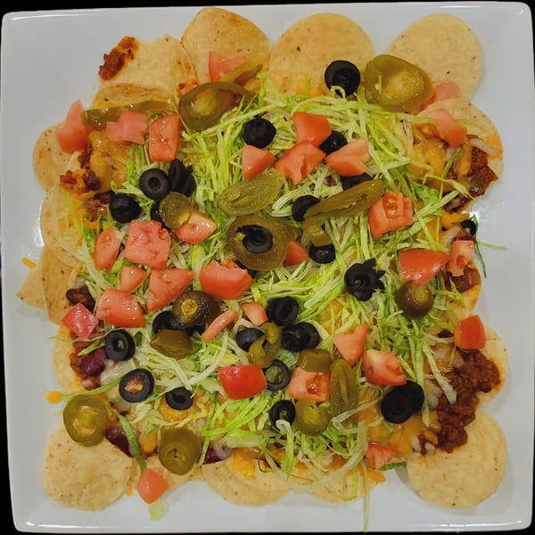 A large plate of Town Pub nachos, topped with shredded lettuce, diced tomatoes, black olives, and jalapeños.