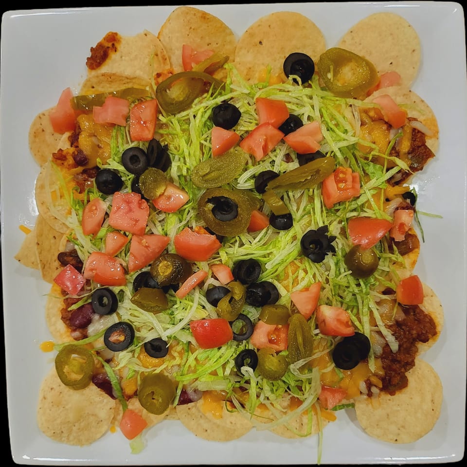 A large plate of Town Pub nachos, topped with shredded lettuce, diced tomatoes, black olives, and jalapeños.