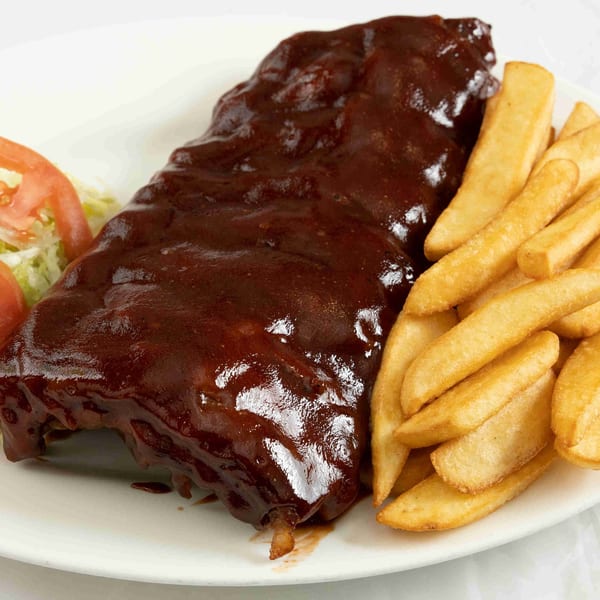 A rack of BBQ ribs with a side of golden french fries and a small salad.