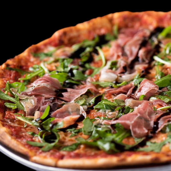 Close-up of a Town Pub pizza topped with prosciutto, arugula, and balsamic glaze.