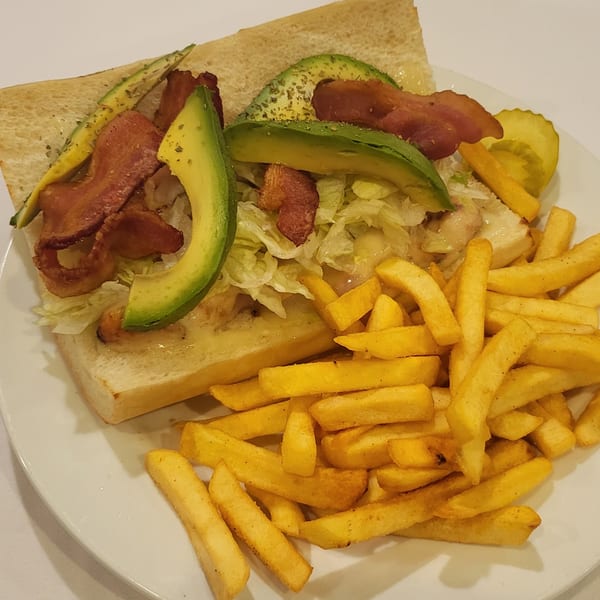 A Town Pub sandwich with bacon, avocado, and lettuce, served with golden french fries and a pickle.