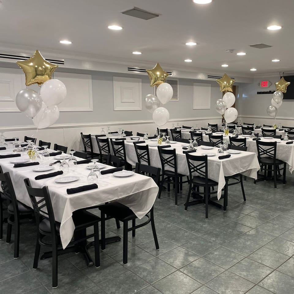 A Town Pub dining room set for a party with white tablecloths, black chairs, and star balloons.