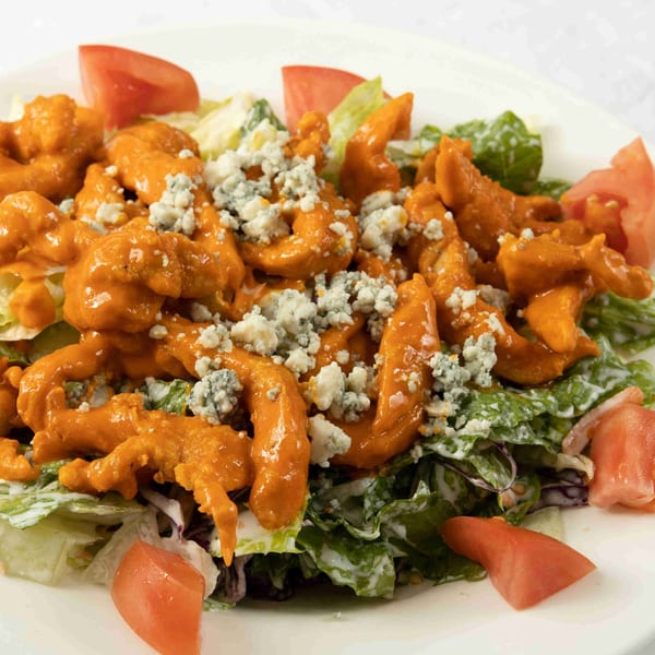 Buffalo chicken salad with blue cheese crumbles, lettuce, and tomato wedges on a white plate.