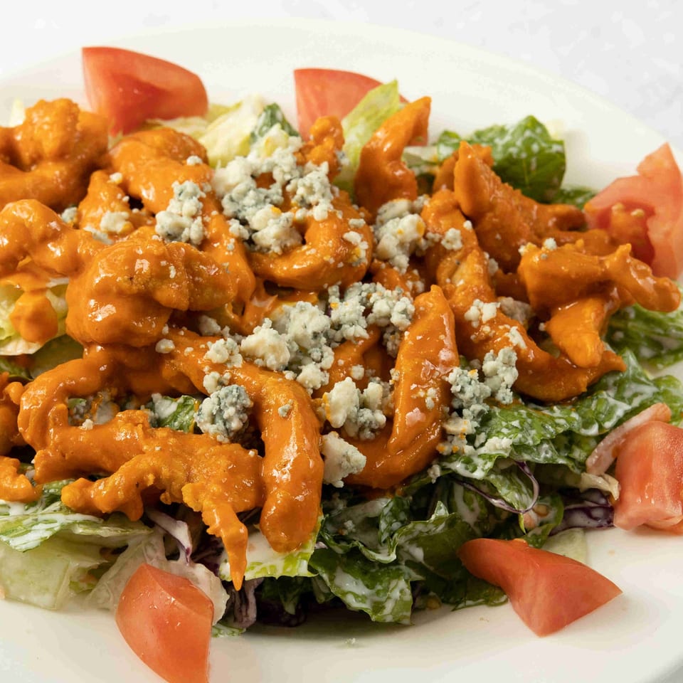 Buffalo chicken salad with blue cheese crumbles, lettuce, and tomato wedges on a white plate.