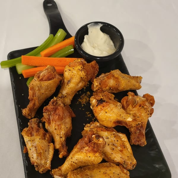 Golden-brown chicken wings with celery, carrots, and ranch dip on a black serving board.