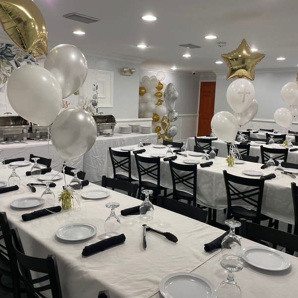 A decorated dining room at Town Pub with white tablecloths, black chairs, and white and gold balloons.