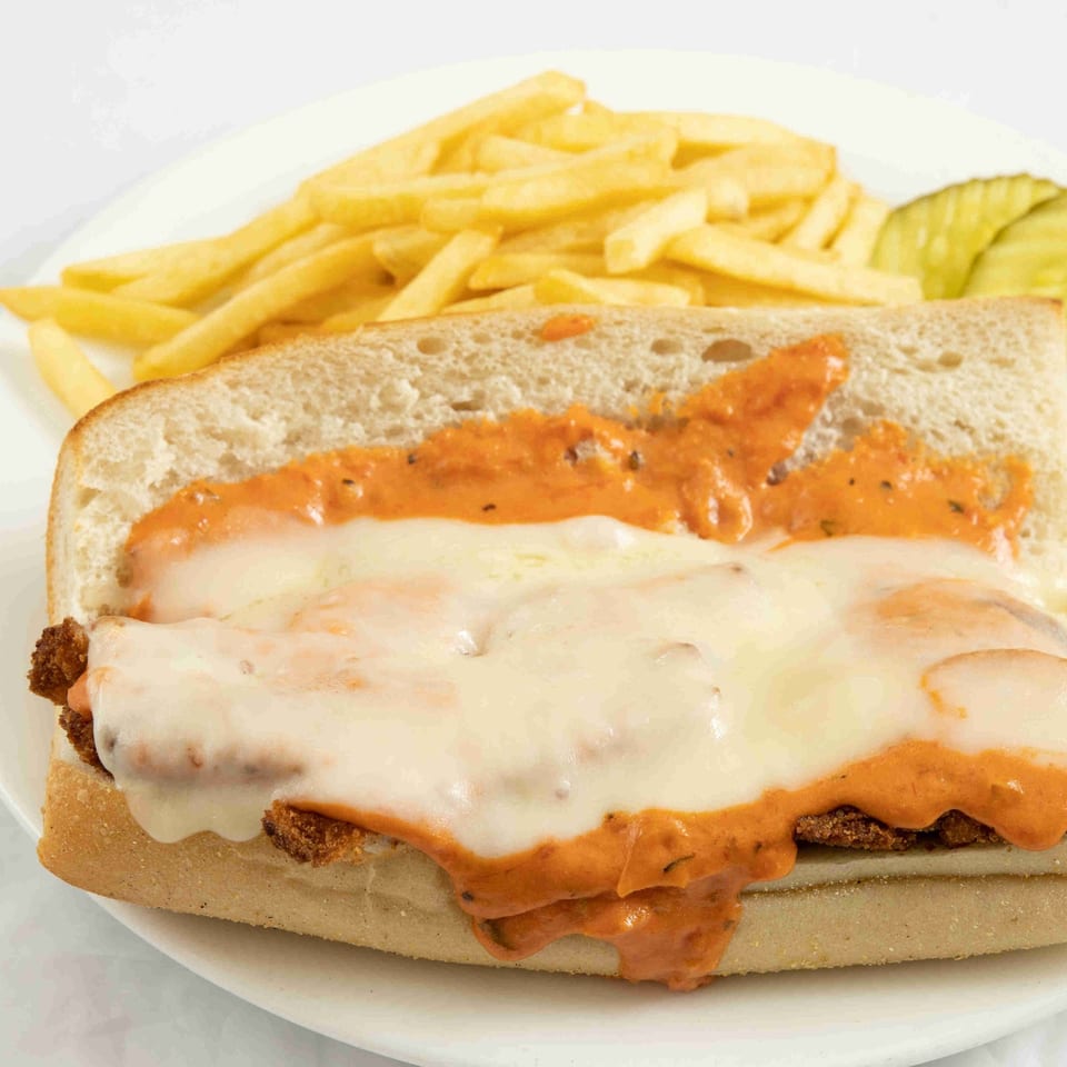 Chicken parmesan sub with melted cheese and red sauce, served with fries and a pickle.