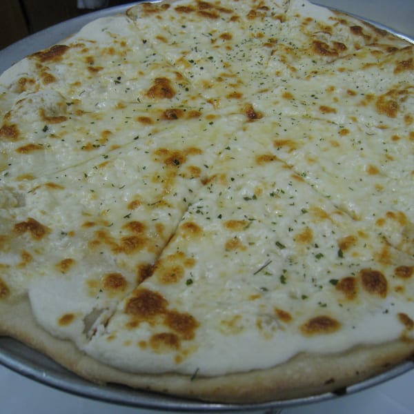 A close-up of a freshly baked white pizza with melted cheese and herbs, sliced and ready to eat.