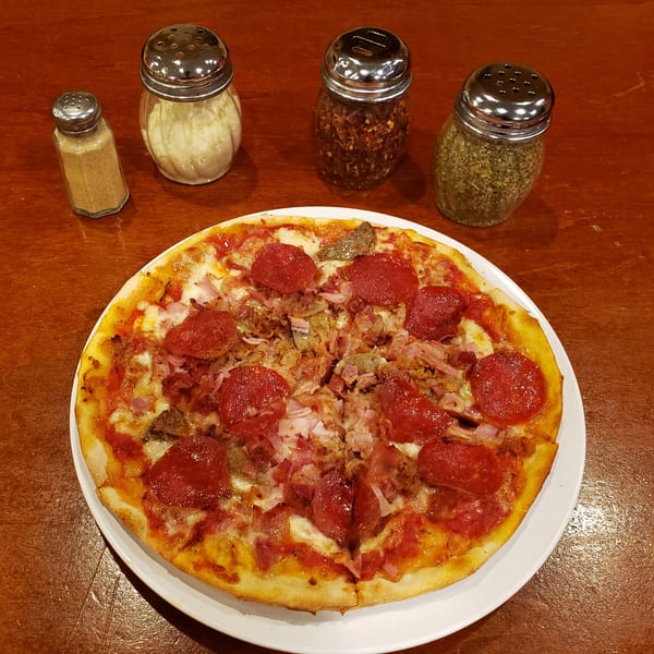 A Town Pub pizza with pepperoni, sausage, and ham, alongside shakers of cheese and spices.