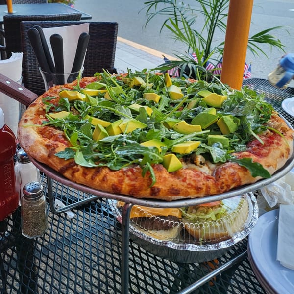 A Town Pub pizza with arugula and avocado on a metal stand on an outdoor patio table.