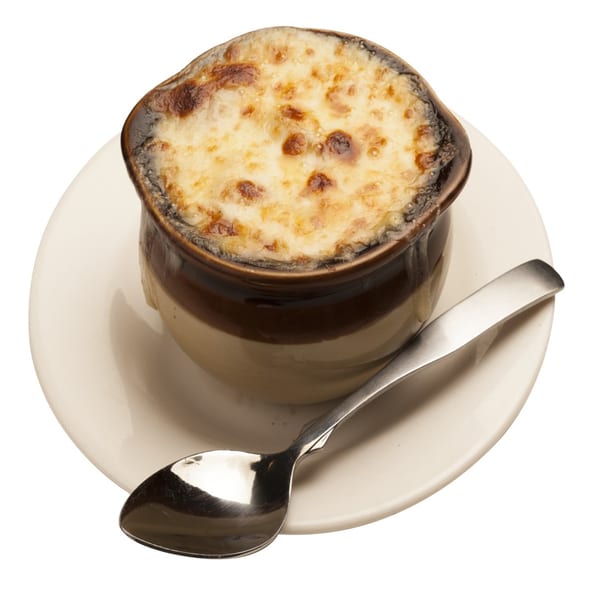 French onion soup in a brown crock with melted, bubbly cheese on top, served with a spoon.