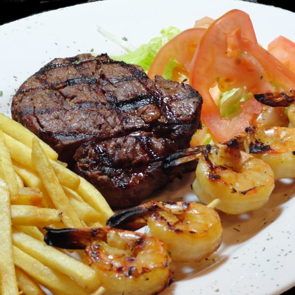 Grilled steak, shrimp skewers, french fries, and a side salad on a white plate.